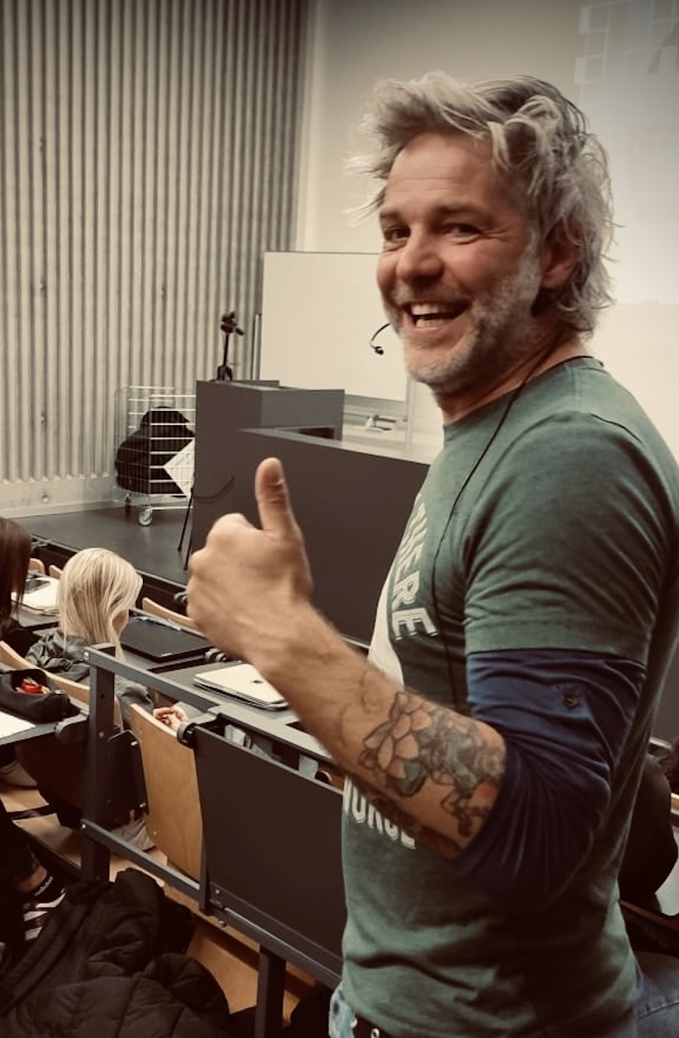 Robin in a lecture hall with his headset on, grinning and giving a big thumbs up