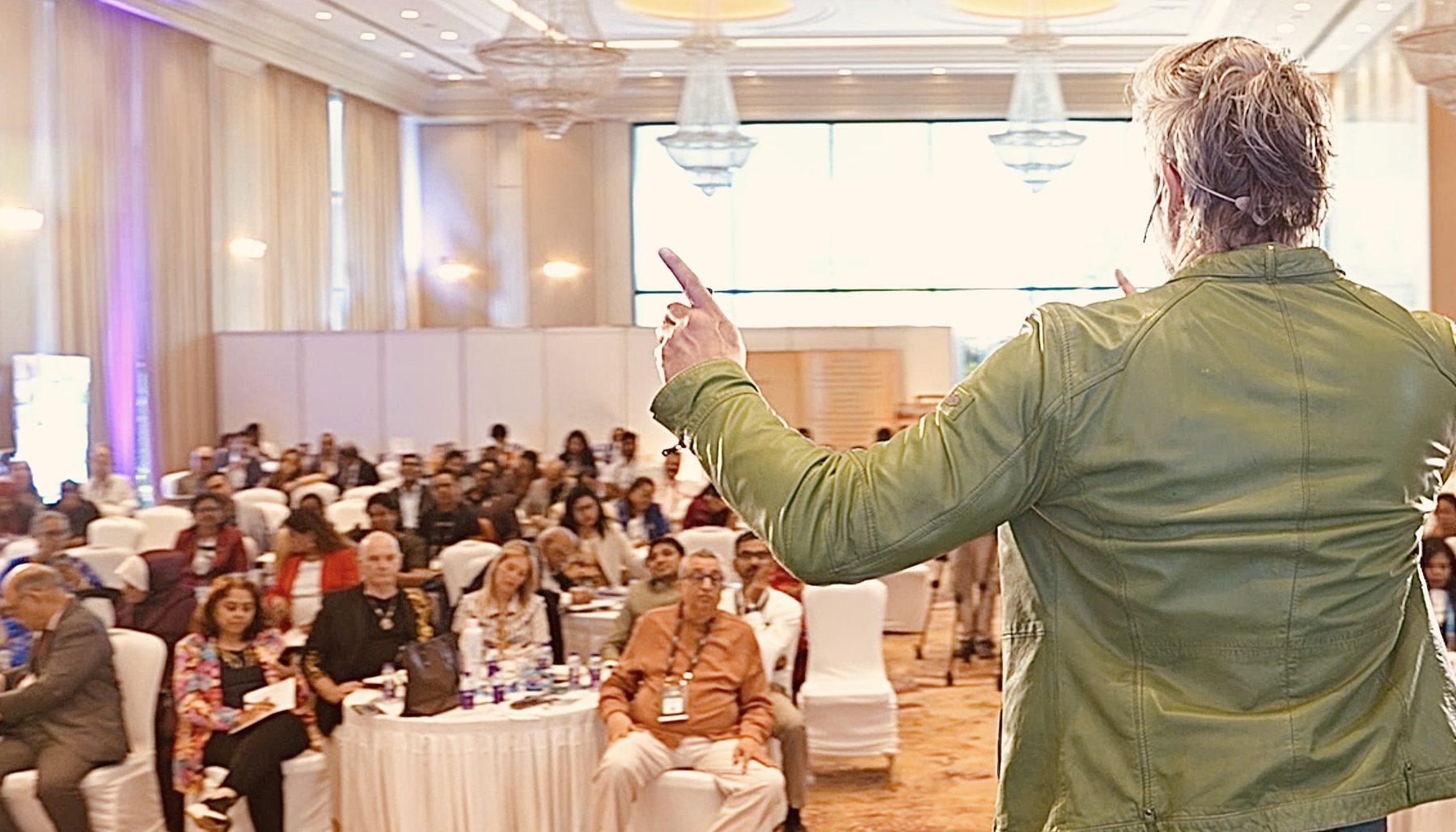 Robin seen from behind, on stage in front of a full ballroom in Chennai