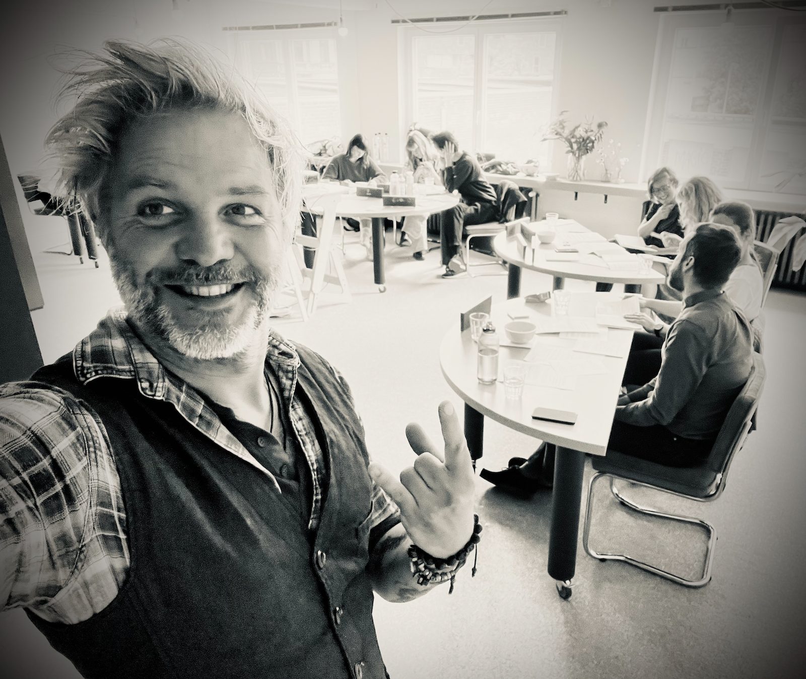 Robin giving a rock hand in a selfie while teams work on their brand flaws at round tables