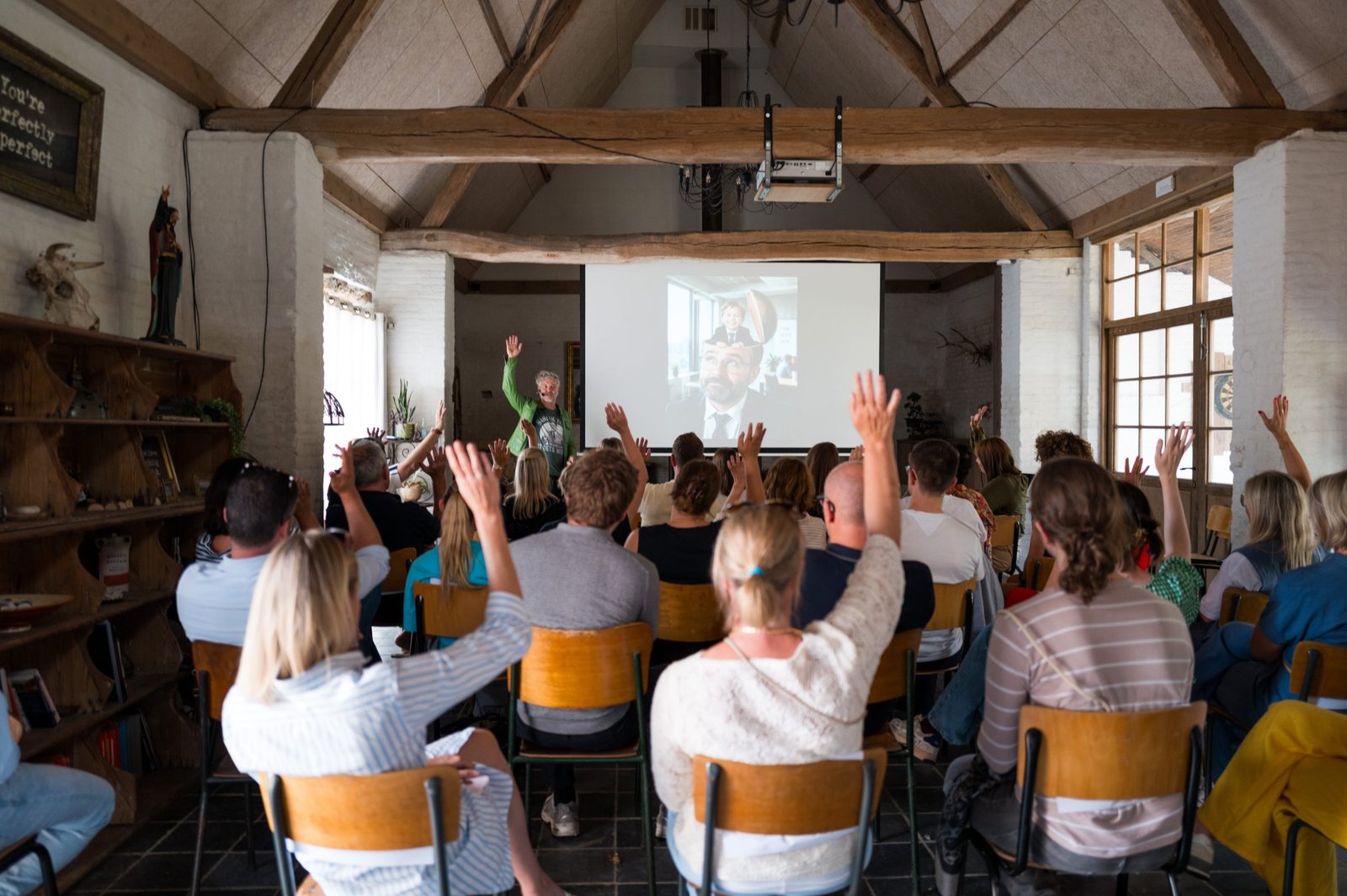 A full house raising their hands during Robin's keynote in the barn at Boereau, under old oak beams